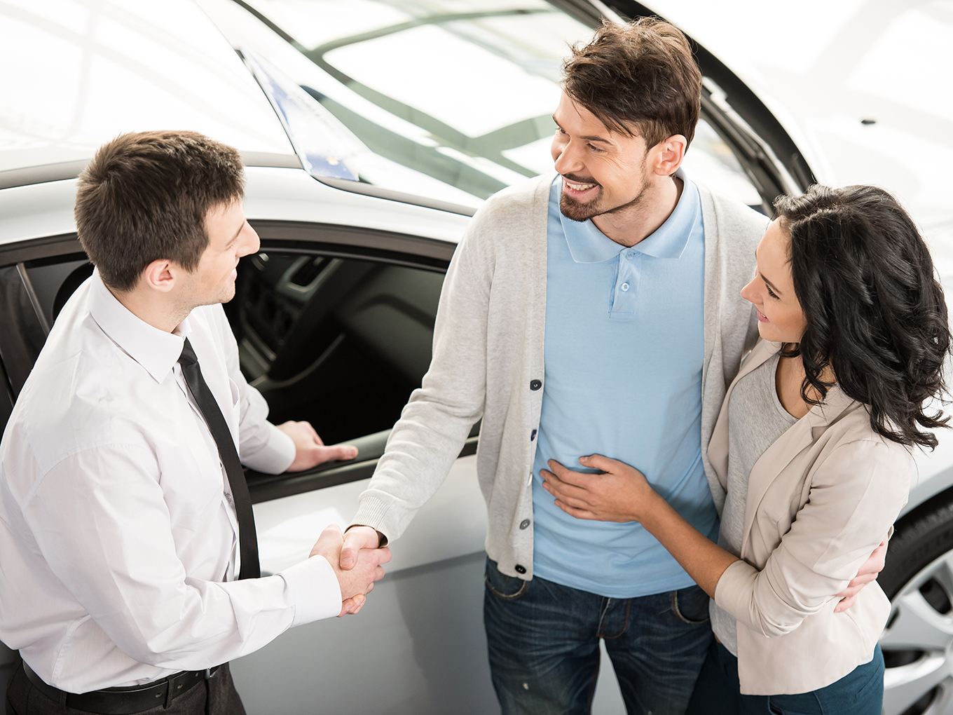 Approval Heroes connects you with trusted car dealers for a stress-free car-buying experience. Car salesman shaking hands with happy couple in showroom