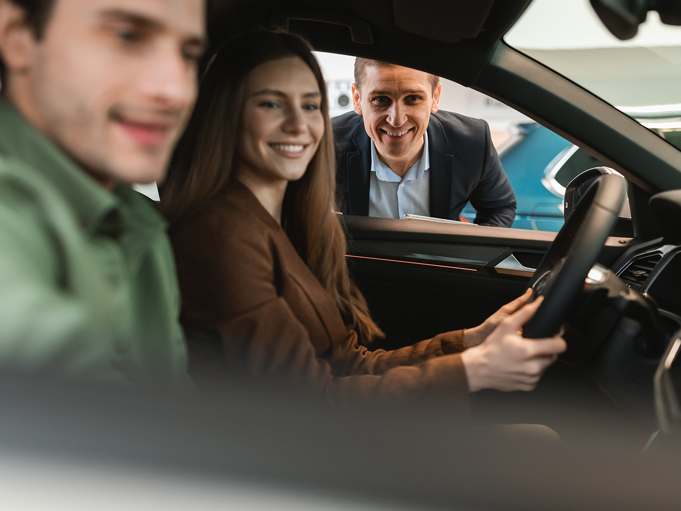 Find your dream car with Approval Heroes Young couple sitting in a new car at a dealership talking to a Car salesman
