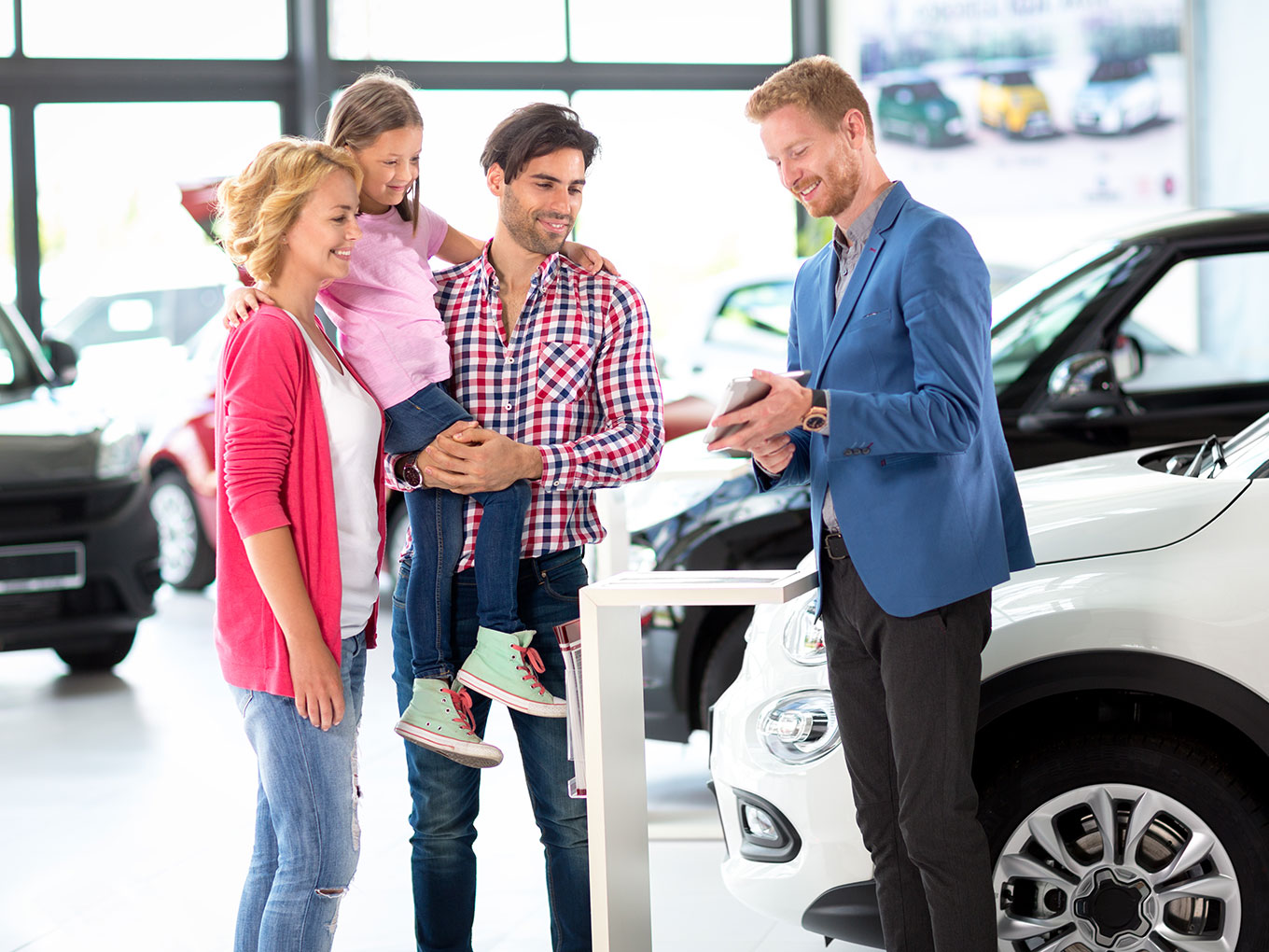 A professional car dealer assisting a family in a dealership showroom, presenting a stylish vehicle and explaining the car loan process.