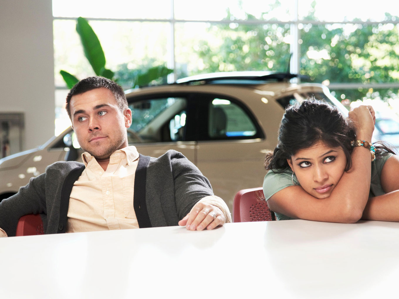A frustrated couple sitting in a car showroom, reflecting the consequences of making mistakes with auto loans