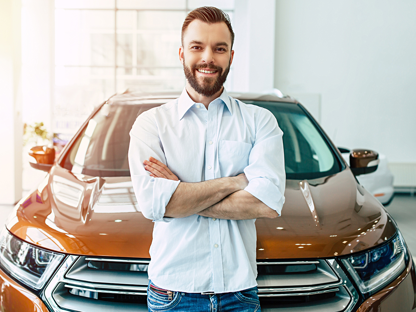 Happy Confident Car Buyer Younger Man with beard smilling and standing in from of newly purchased vehicle.