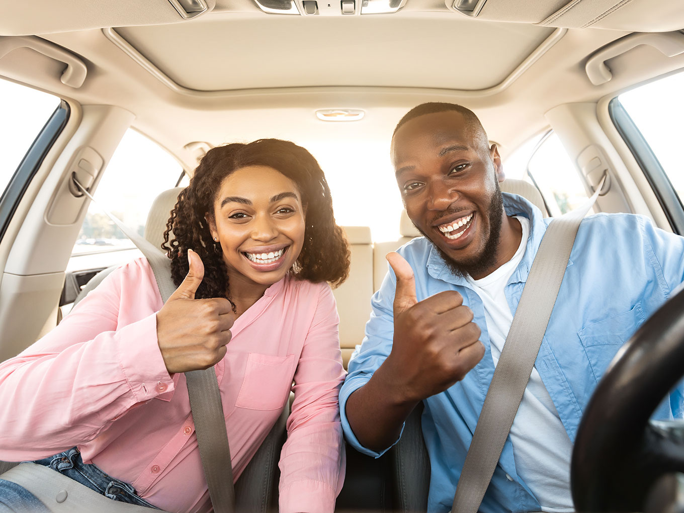 A happy couple sitting inside a car, viewed from the front windshield, gesturing thumbs up in approval. They express satisfaction and joy, representing the positive car-buying experience and the trust in Approval Heroes' services.