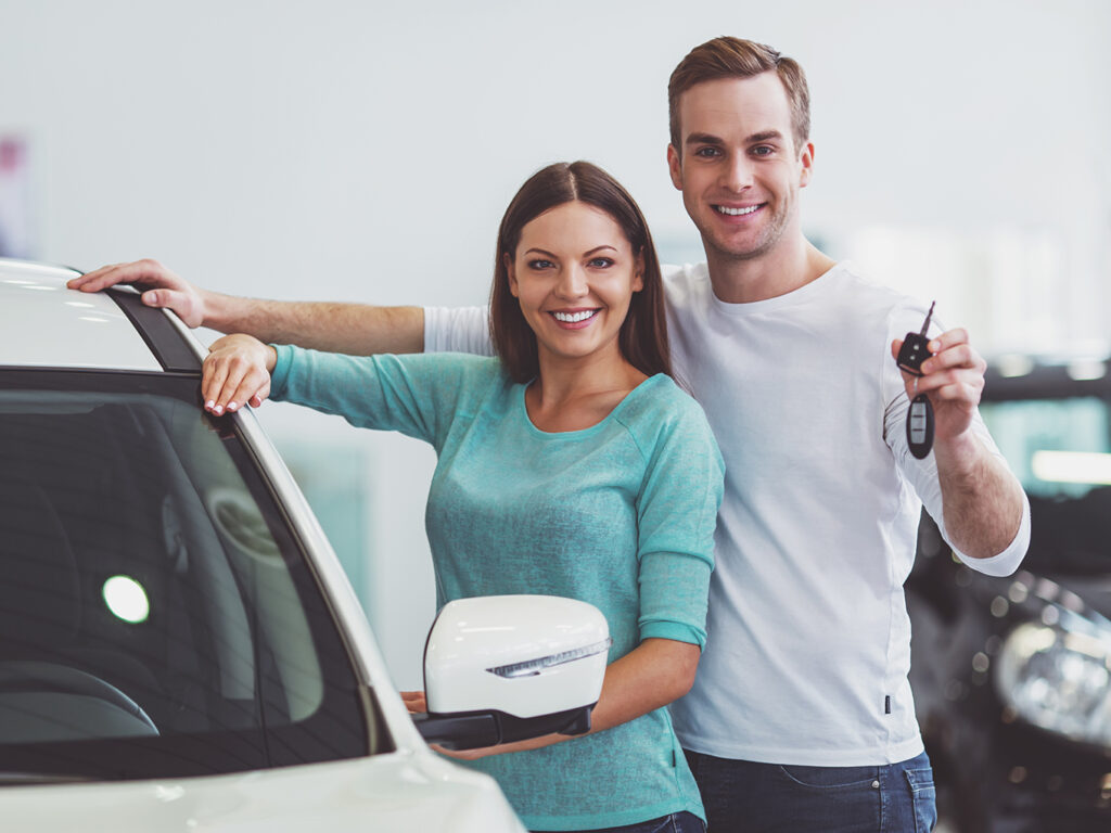 Happy couple standing in front of a new car smiling and holding key