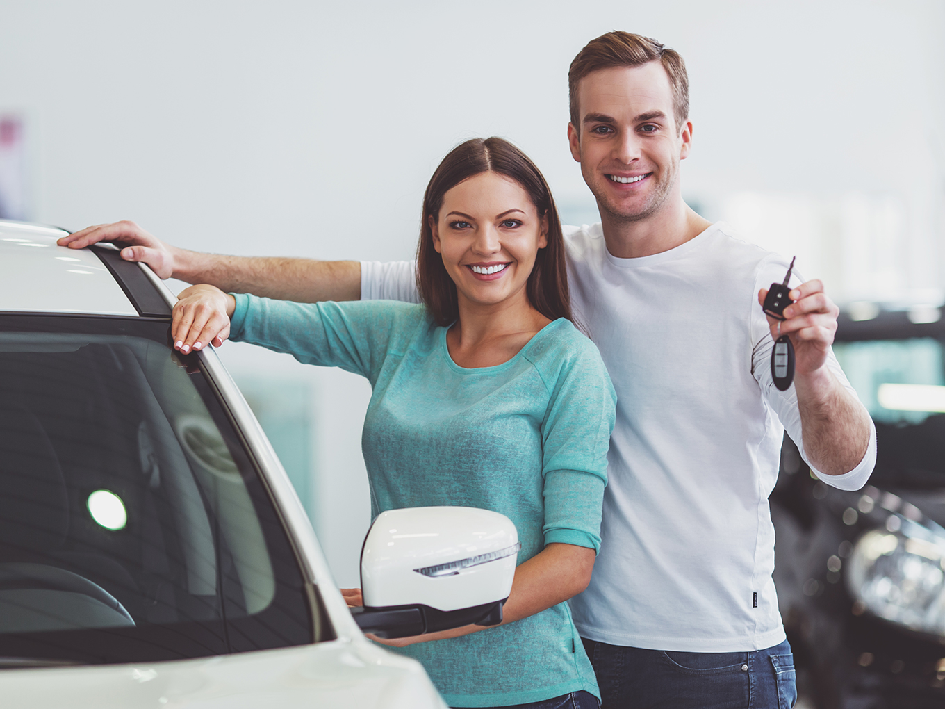 Happy couple standing in front of a new car smiling and holding key