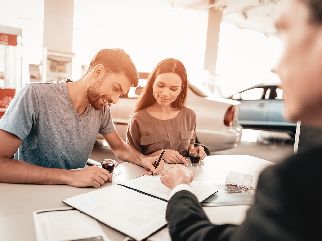 Happy customer signing car loan documents A smiling customer signing car loan documents with an Automotive Consultant sitting across from them at a desk.