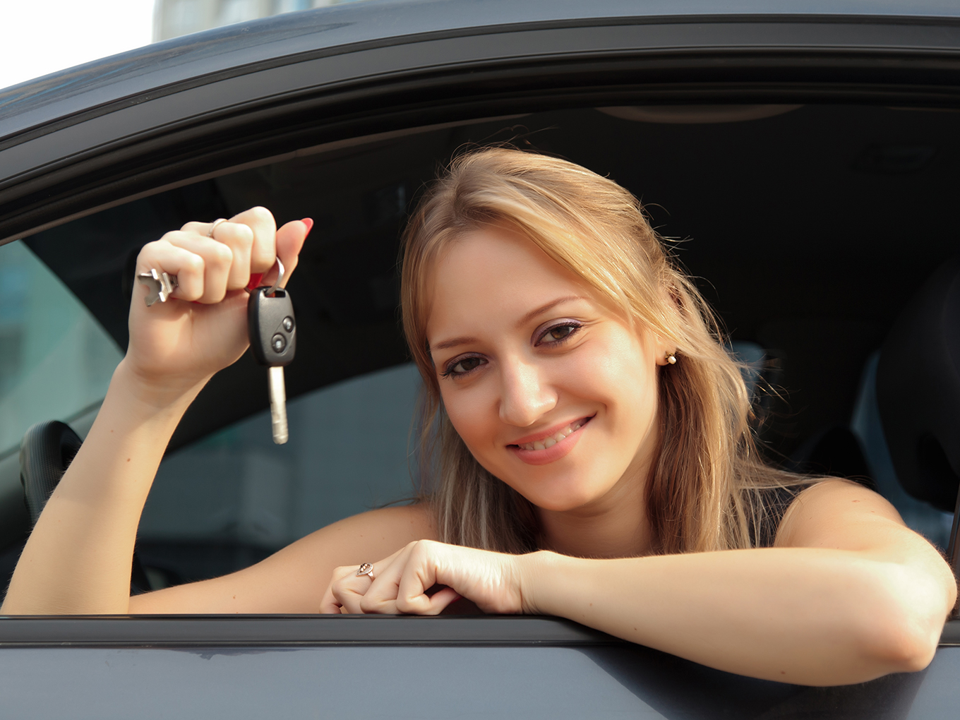 Happy Customer with Car Young happy woman in newly purchased car holding up key from drivers side looking out the vehicle window at the camera
