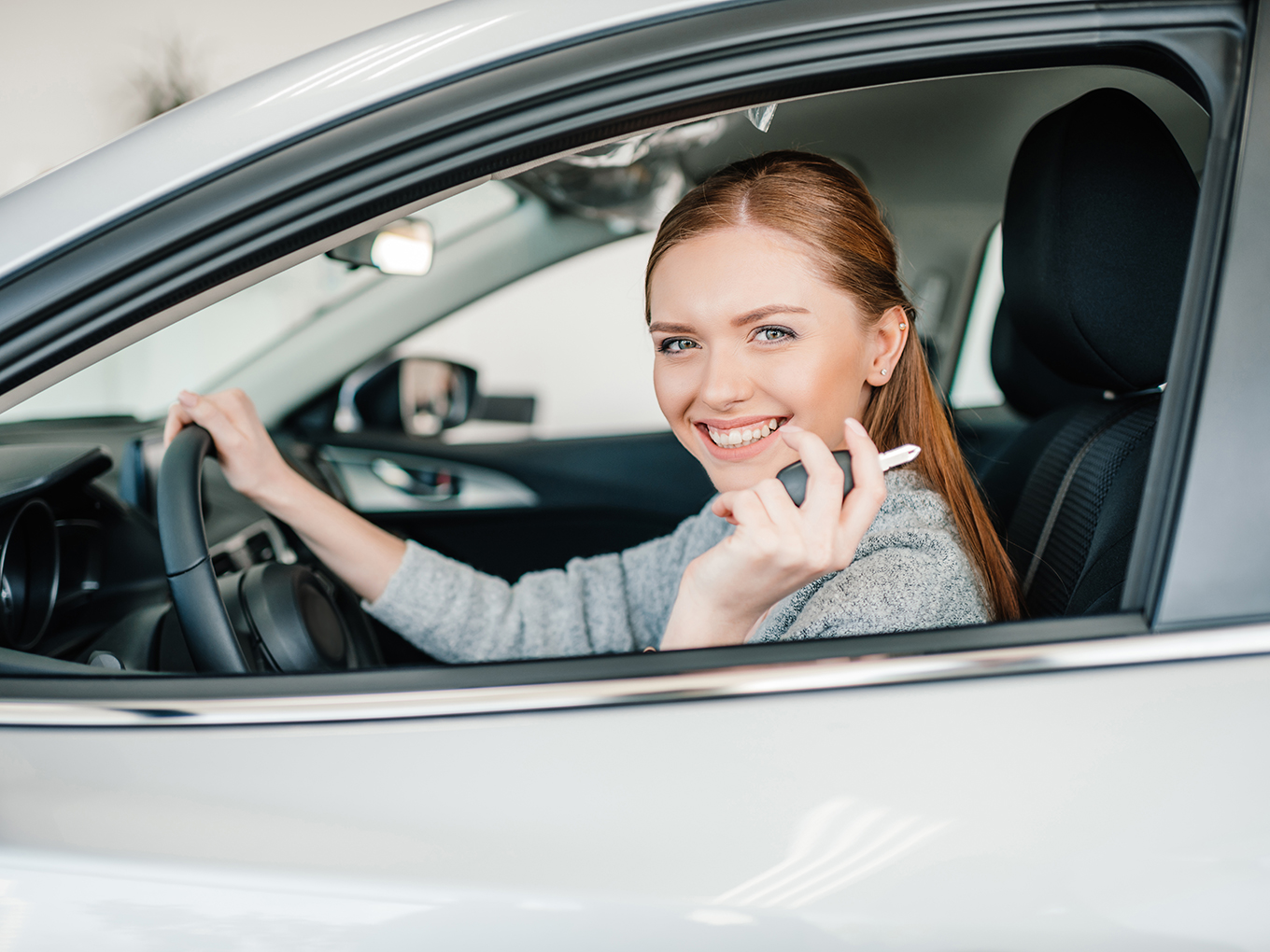 Happy customer holding car key in the driver's seat of a new car, symbolizing Approval Heroes' car loan services.