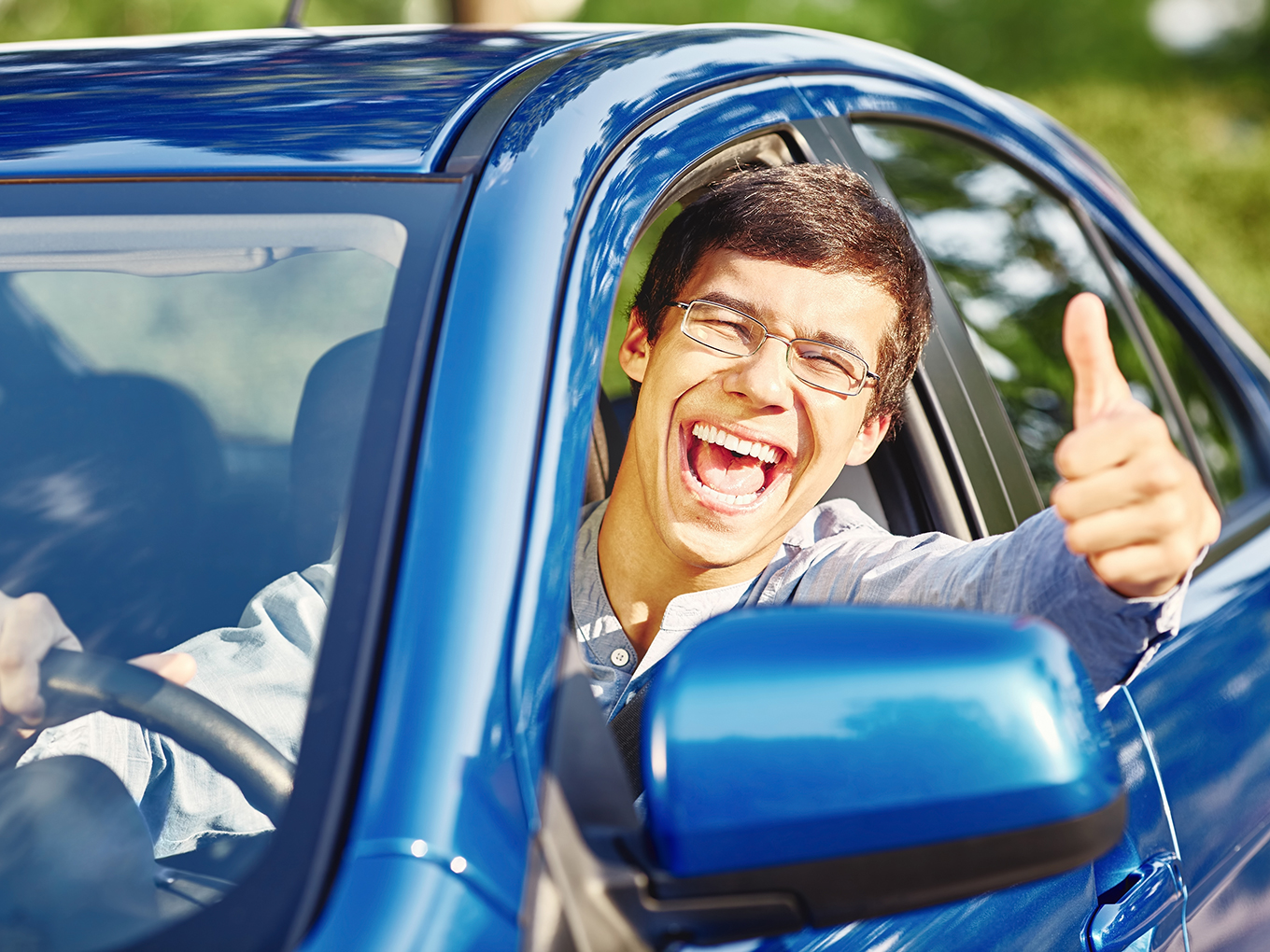 A joyful young man with a smile and thumbs up, enjoying the freedom of driving his car after successfully paying off his car loan.