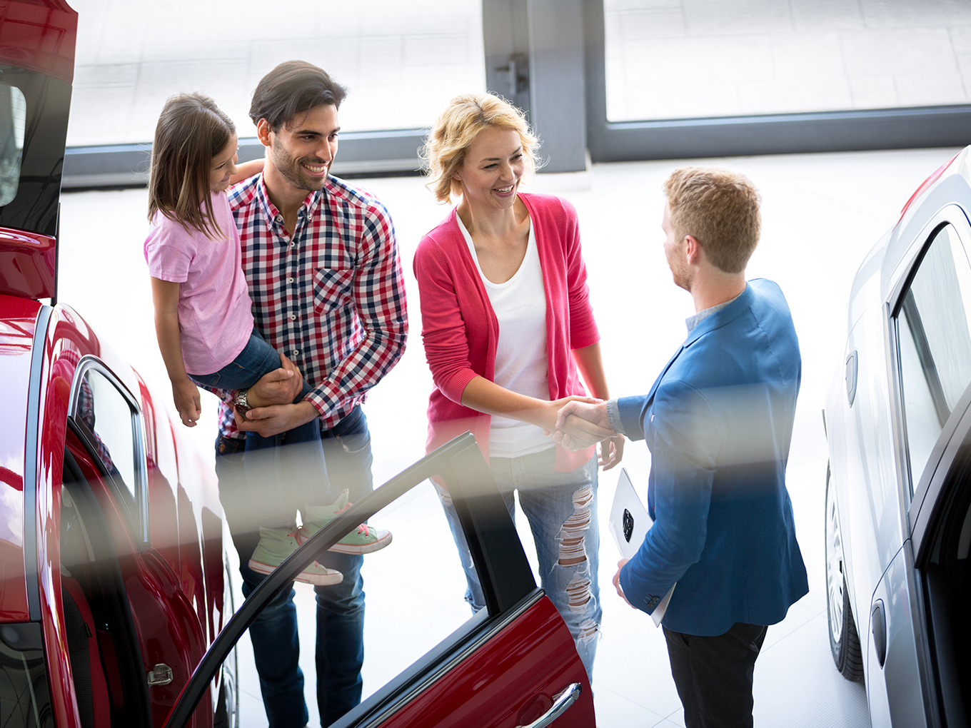 a happy couple with a car salesperson in a dealership showroom