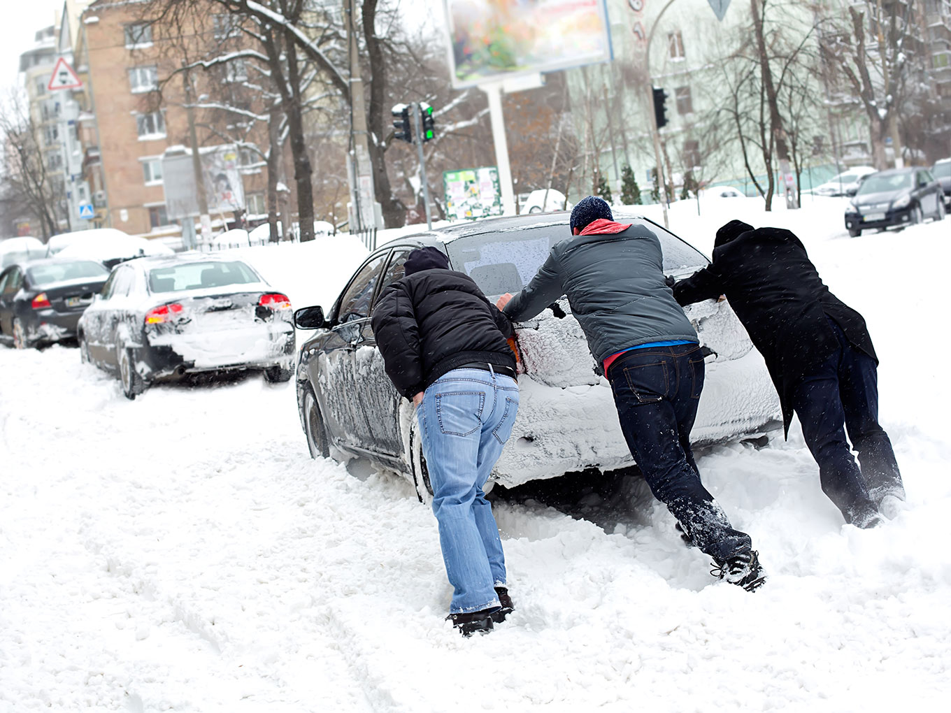 Join a team that makes a difference A group of people pushing a car that is stuck in the snow.