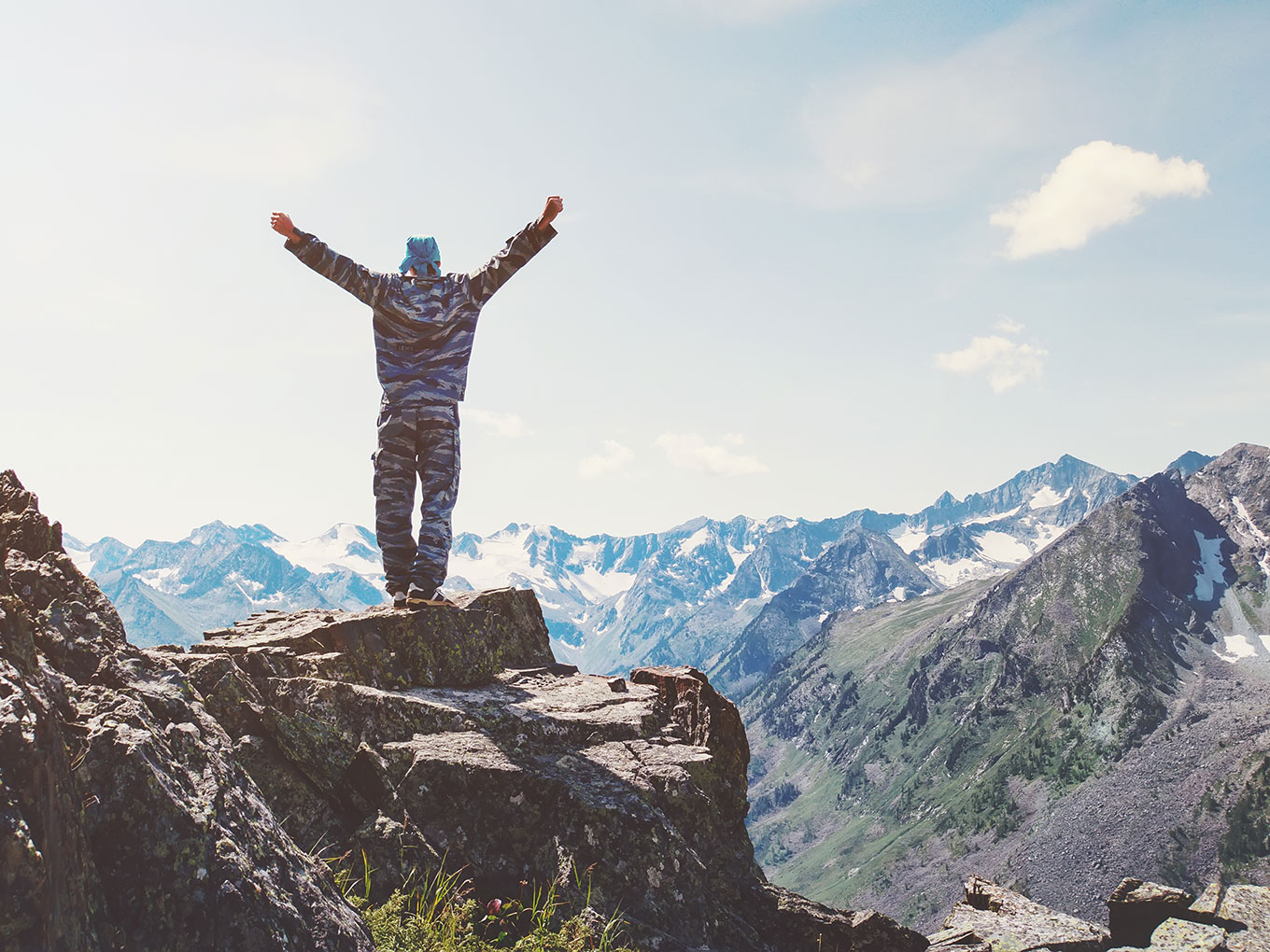Climb to new heights with us A yooung man standing on top of a mountain overlooking the scenery.