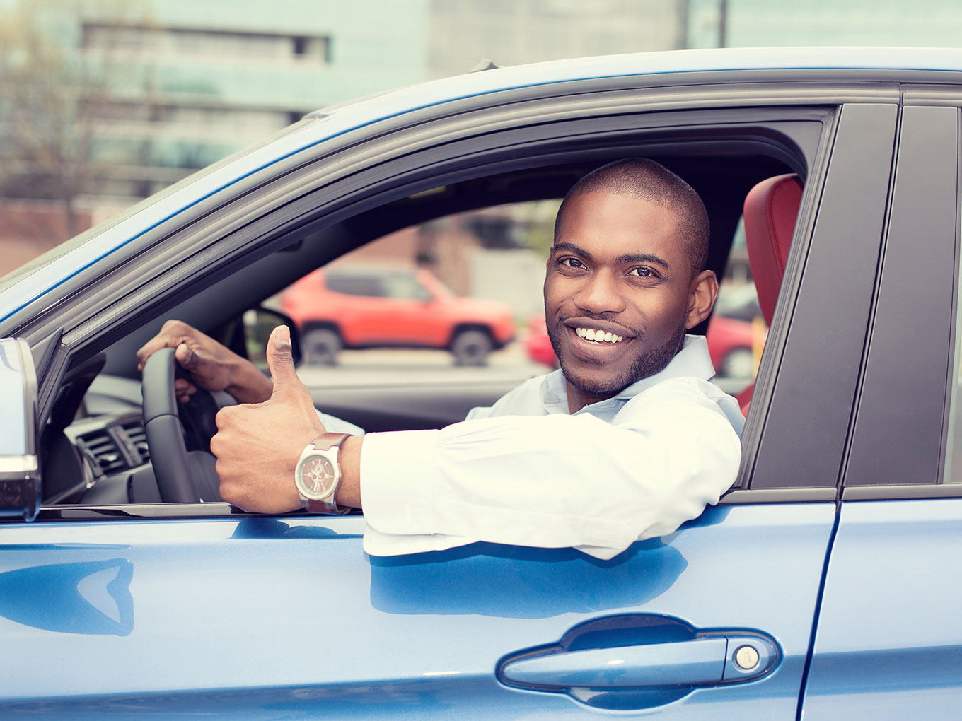 A smiling man sitting in the driver’s seat of a car, giving a thumbs-up, symbolizing confidence and readiness to drive.