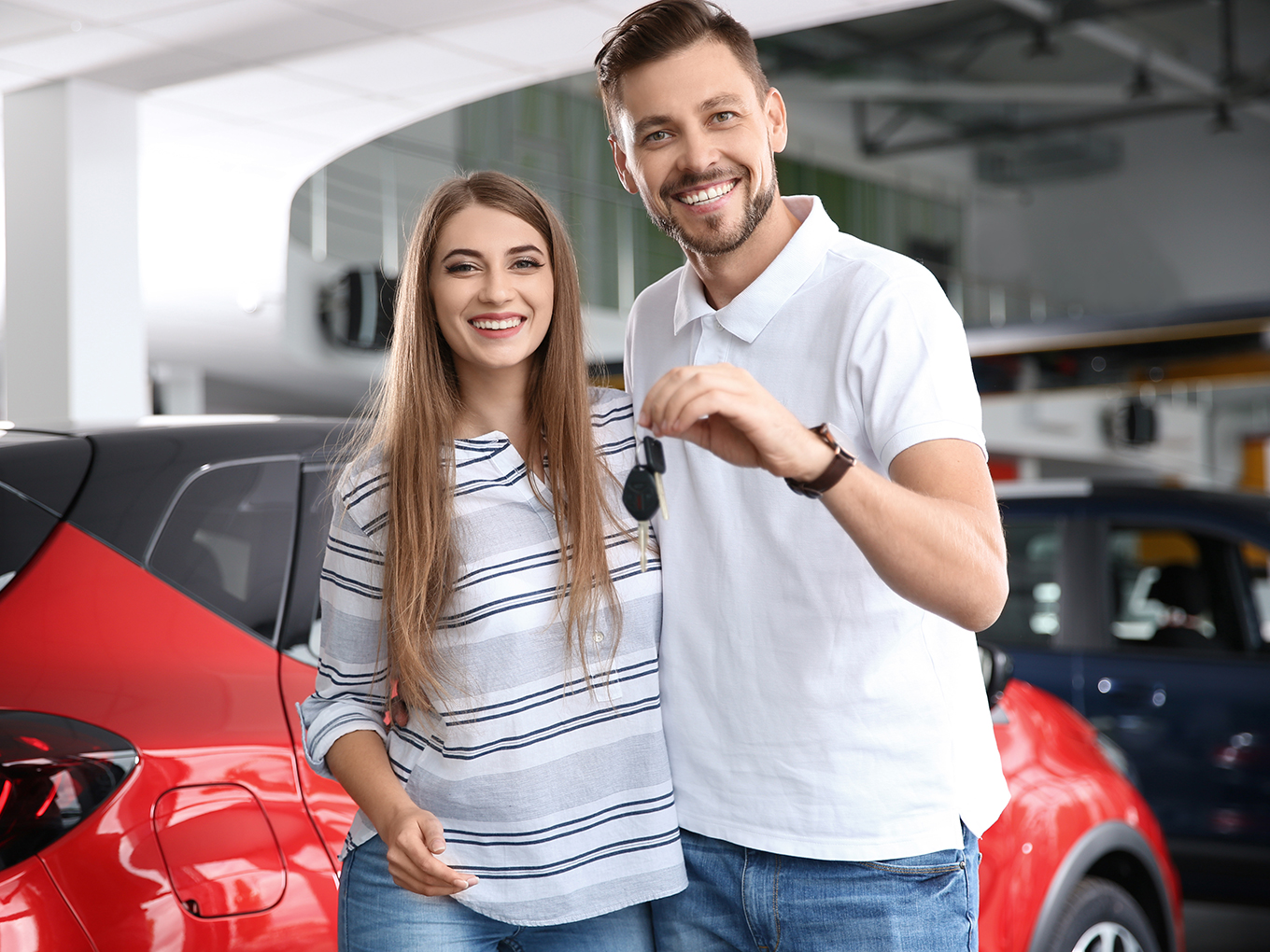 Happy woman and man with car keys in modern auto dealership