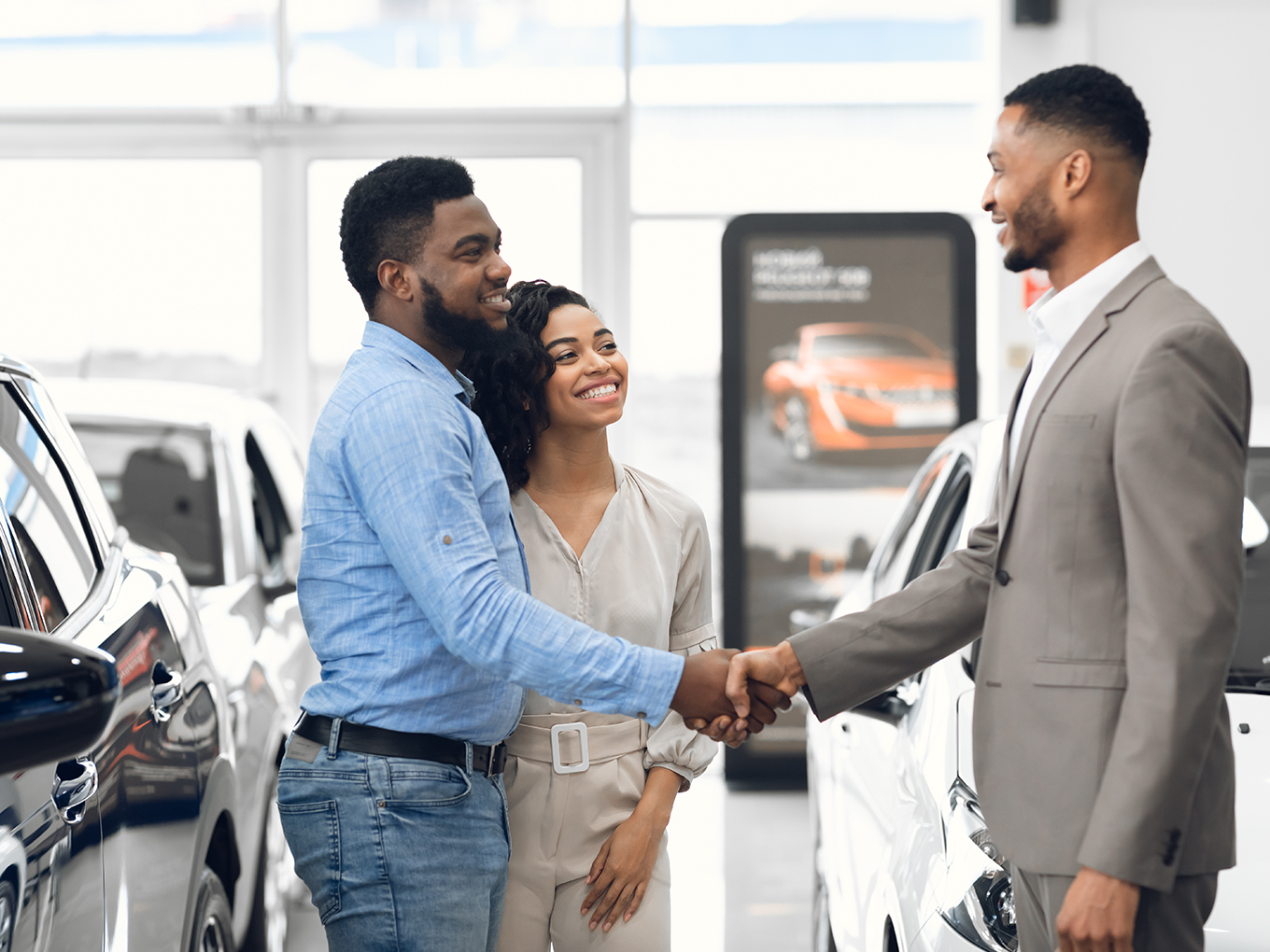 Successful Car Purchase Happy African American couple shaking hands with a car salesman after purchasing a vehicle